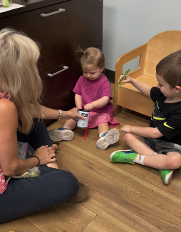 Speech therapist seated on floor with 2 young children in a speech therapy session